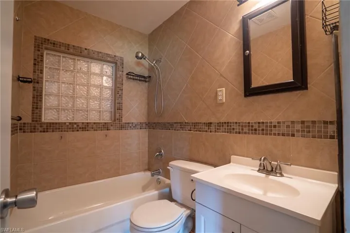 Full bathroom with tile walls, tiled shower / bath combo, toilet, and vanity with extensive cabinet space