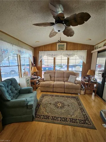 Living area featuring ceiling fan, a textured ceiling, wood finished floors, and wood walls