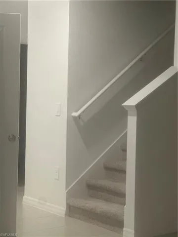 Carpeted staircase with a white handrail, leading from a tiled floor entry