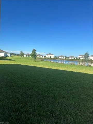 Expansive lawn with a water feature, bordered by distant homes under a clear sky