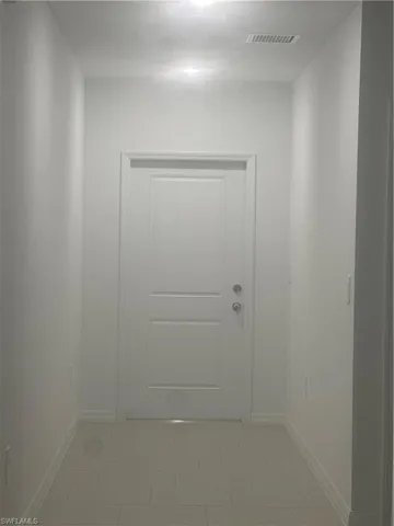 Recessed ceiling lighting illuminating a neutral color palette, featuring a two-panel door with silver-tone hardware and light-toned tile flooring