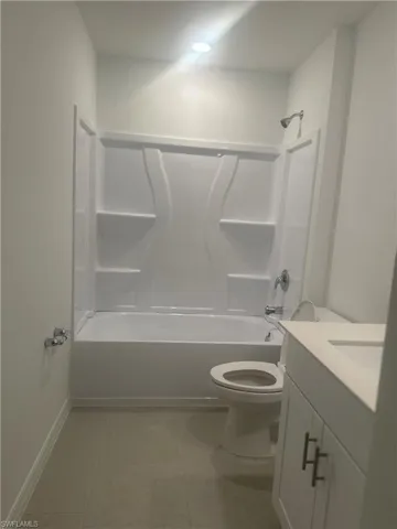 White bathtub with integrated shower, single vanity with white cabinetry and dark hardware, white toilet, and recessed ceiling lighting