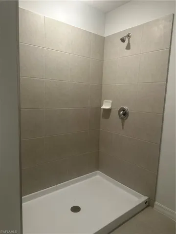 Walk-in shower featuring light-toned wall tiling, a white shower pan, and a chrome shower head with coordinating fixtures