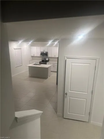 Kitchen with white cabinetry, stainless steel appliances, a center island with sink, and tile flooring