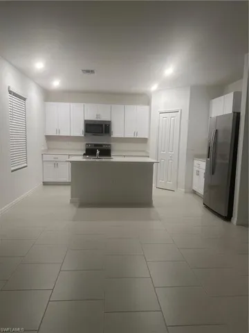 Open-concept kitchen featuring an island, white cabinetry, integrated stainless steel appliances, light-colored countertops, and tile flooring