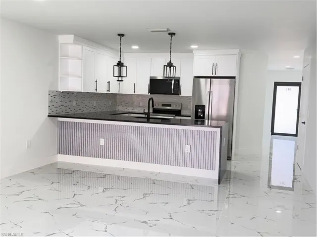 Kitchen featuring dark stone counters, a peninsula, open shelves, stove, and white cabinetry