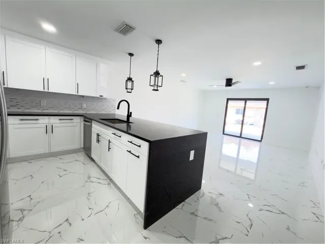 Kitchen featuring a peninsula, dark stone countertops, decorative light fixtures, white cabinets, and light marble finish flooring