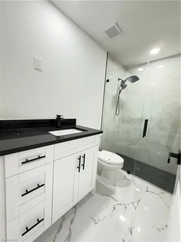 Bathroom featuring vanity, a marble finish shower, light marble finish floors, and recessed lighting