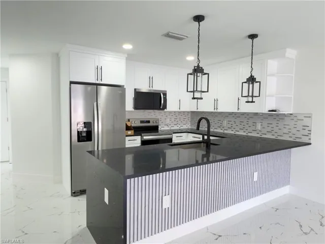 Kitchen with dark stone counters, a peninsula, stainless steel appliances, light marble finish flooring, and open shelves