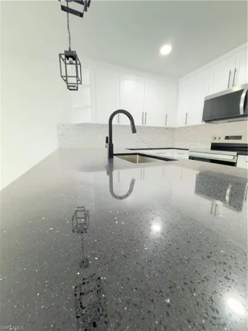 Kitchen view of white cabinets, light stone counters, range, and decorative backsplash