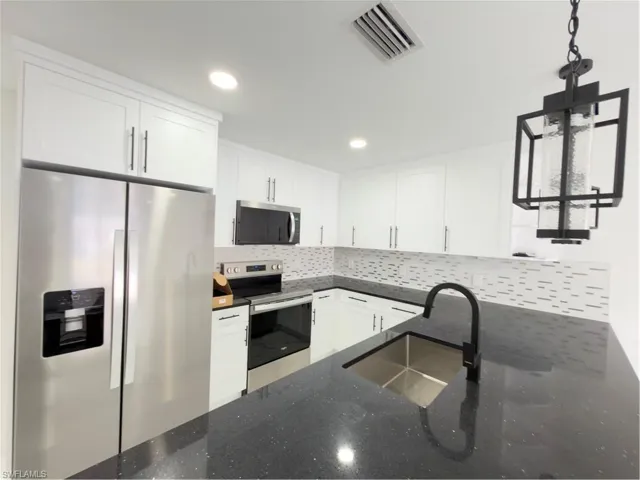 Kitchen featuring refrigerator, white cabinetry, range, and hanging light fixtures