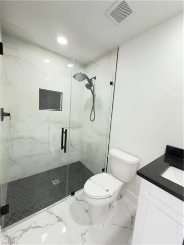 Full bathroom featuring a marble finish shower, vanity, and marble look tile flooring