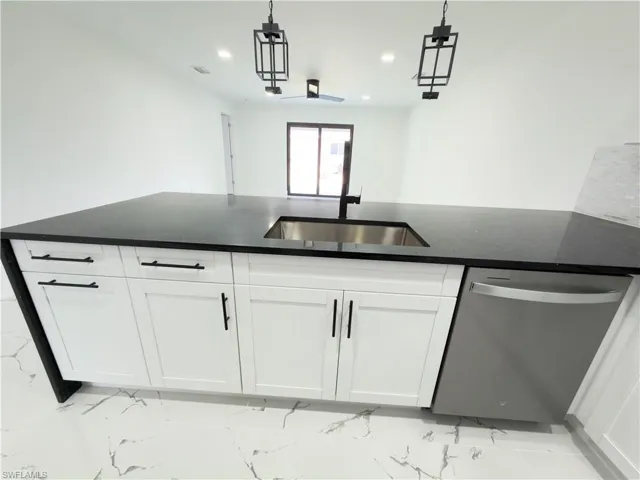 Kitchen featuring stainless steel dishwasher, white cabinets, dark stone counters, and hanging light fixtures