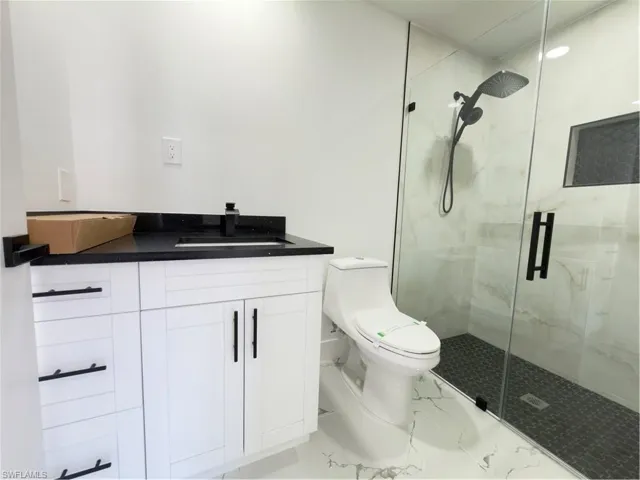 Bathroom featuring vanity, a marble finish shower, and light marble finish floors