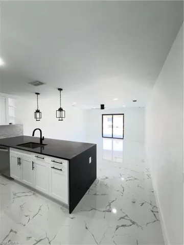 Kitchen featuring white cabinets, open shelves, dishwasher, dark stone countertops, and hanging light fixtures