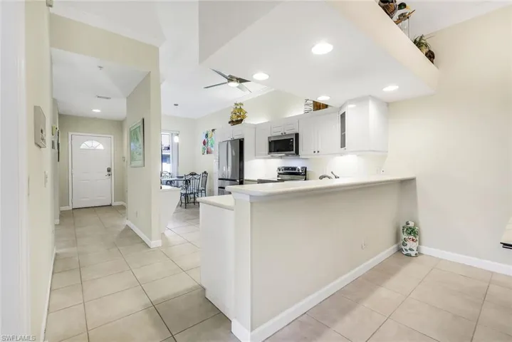 Kitchen with white cabinets, light tile patterned flooring, a peninsula breakfast bar, appliances with stainless steel finishes and recessed lighting.