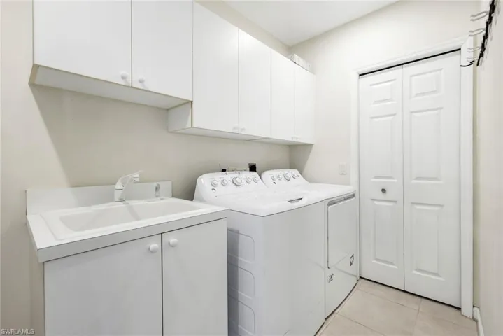 Laundry area featuring cabinet space, Utility sink, light tile patterned floors, with washing machine and dryer.