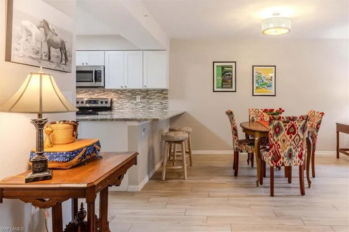 Kitchen featuring decorative backsplash, a kitchen bar, light stone counters, stainless steel appliances, and white cabinetry