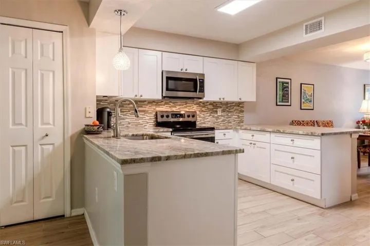 Kitchen featuring a peninsula, light stone countertops, white cabinets, hanging light fixtures, and stainless steel appliances