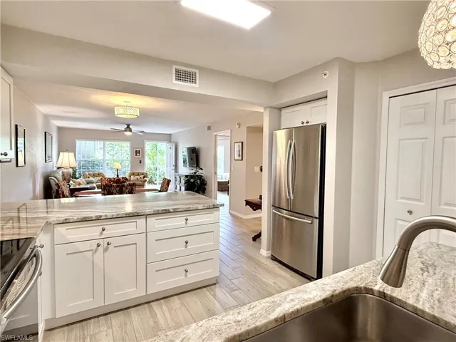 Kitchen with white cabinetry, open floor plan, stainless steel appliances, light stone counters, and a peninsula