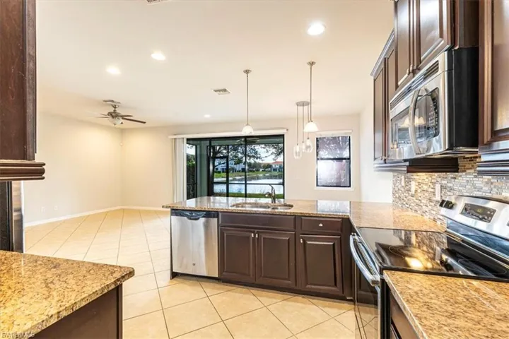 Kitchen featuring stainless steel appliances, dark wood finish cabinetry, and light stone counters