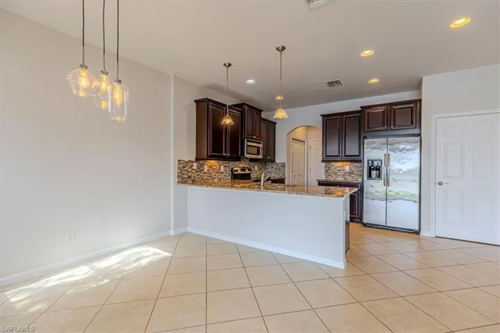 Kitchen with arched walkways, dark wood finish cabinets, stainless steel appliances, light stone counters, and pendant lighting