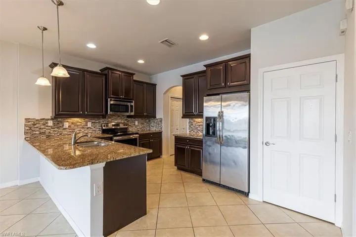 Kitchen with arched walkways, stainless steel appliances, dark wood finish cabinetry, dark stone counters, and a peninsula