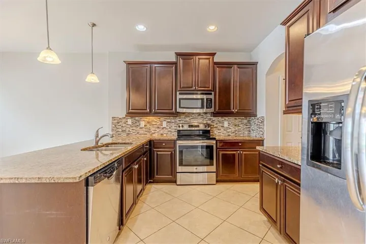 Kitchen featuring stainless steel appliances, light stone counters, decorative light fixtures, a peninsula, and decorative backsplash