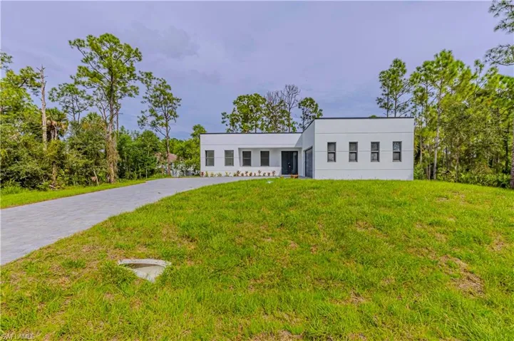 Modern architecture with a white exterior, paver driveway, and surrounding nature trees