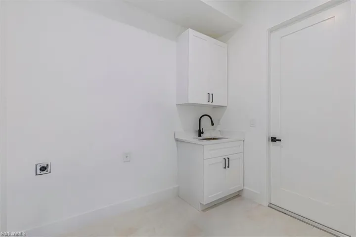 White shaker-style cabinetry with matte black hardware, integrated utility sink with a matte black faucet, light-toned flooring, and a modern interior door with black hardware