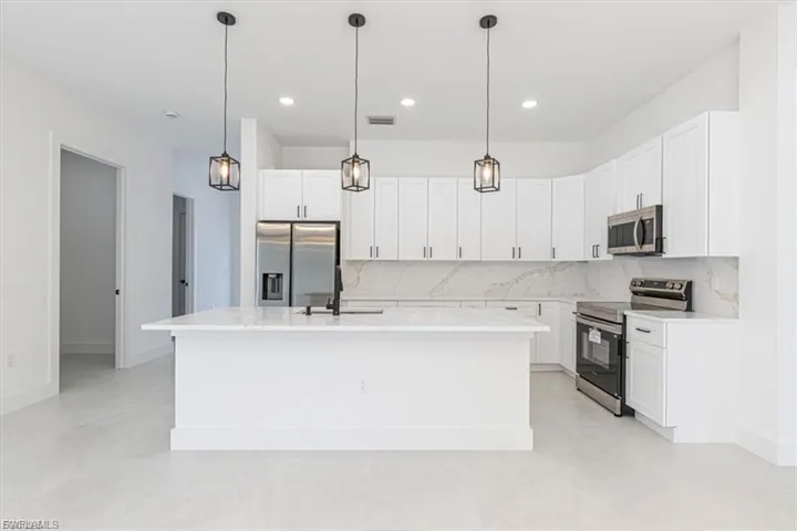 White shaker-style cabinetry, stainless steel appliances, white stone countertops, recessed lighting, and pendulum light fixtures