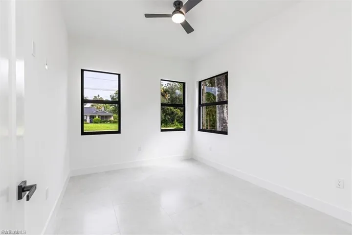 White walls with clean-lined baseboards, three black-framed windows, a ceiling fan with integrated lighting, and light-toned tile flooring