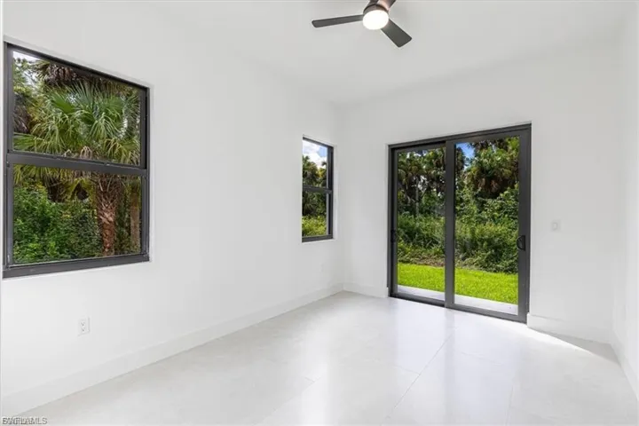 White tile flooring, sliding glass door, multiple windows, ceiling fan, and white walls