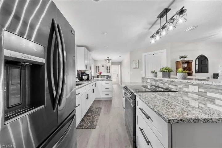 Kitchen with white cabinets, appliances with stainless steel finishes, backsplash, light wood-type flooring, and light stone counters