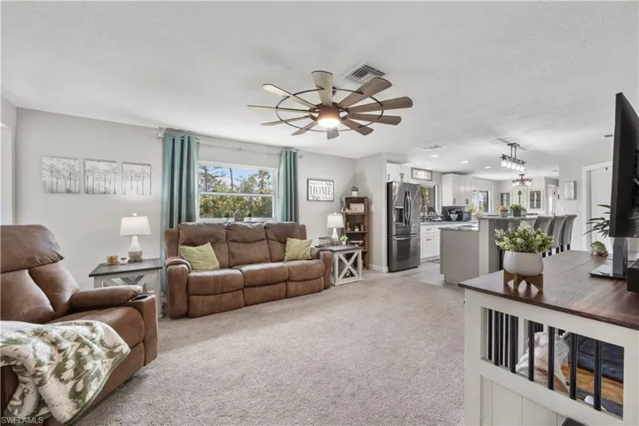 Carpeted living room with ceiling fan with notable chandelier and a textured ceiling