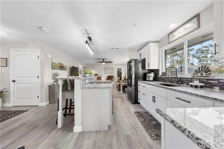 Kitchen with tasteful backsplash, white cabinets, sink, light stone counters, and a breakfast bar area