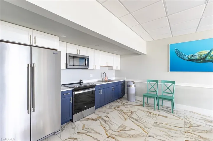 Kitchen featuring stainless steel appliances, blue cabinetry, light marble finish flooring, light countertops, and white cabinets