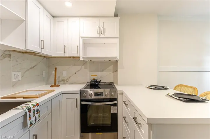 Kitchen with stainless steel range with electric stovetop, light countertops, white cabinetry, and decorative backsplash