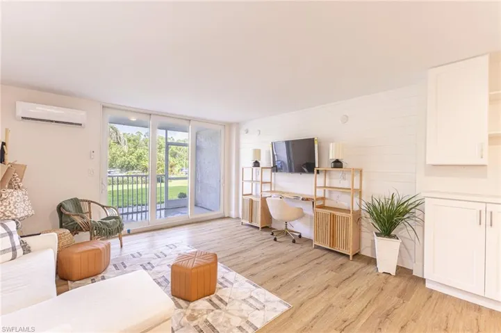 Living room featuring light wood-type flooring, a desk, a wall unit AC, and floor to ceiling windows