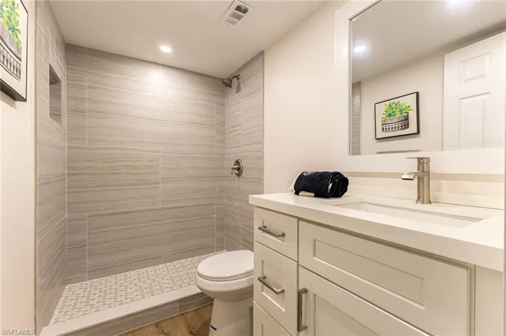 Full bathroom featuring vanity, tiled shower, recessed lighting, and wood finished floors