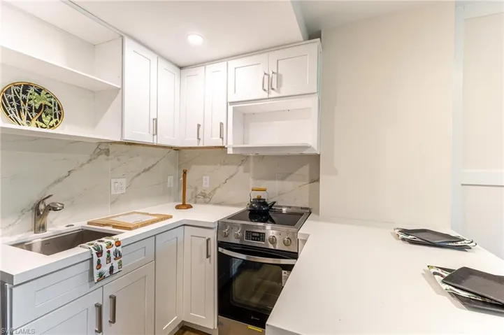 Kitchen featuring open shelves, electric range, light countertops, decorative backsplash, and white cabinets