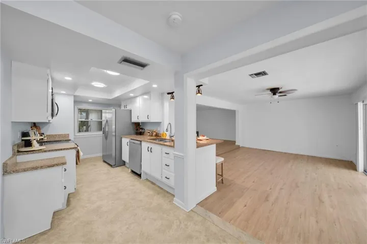 Kitchen with white cabinets, a raised ceiling, a breakfast bar, open floor plan, and recessed lighting