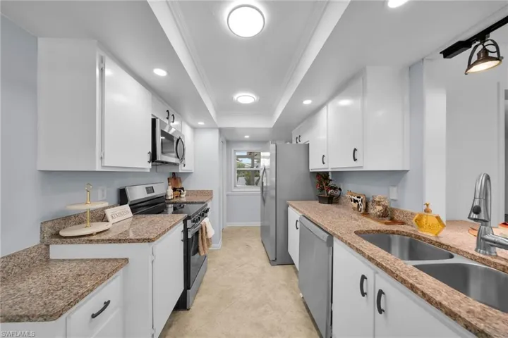 Kitchen with appliances with stainless steel finishes, a raised ceiling, white cabinetry, ornamental molding, and light stone counters