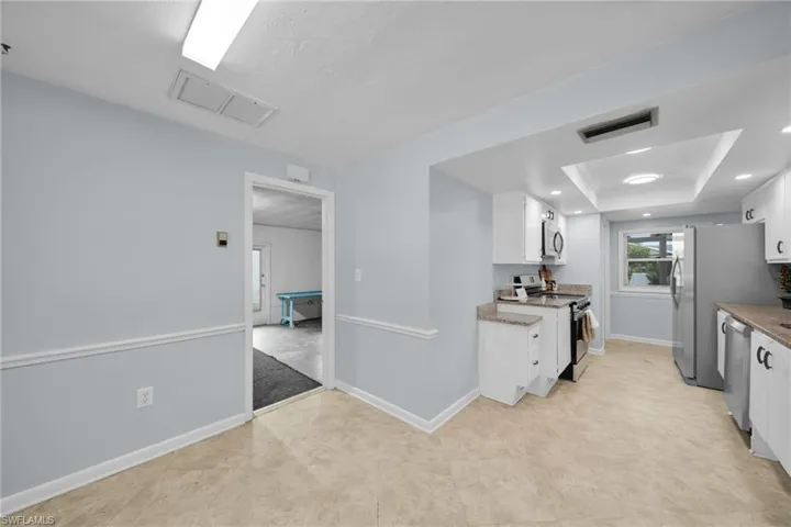 Kitchen featuring white cabinets, appliances with stainless steel finishes, a raised ceiling, and light stone countertops
