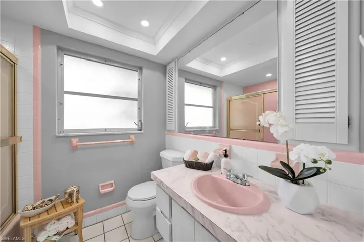 Full bath featuring a shower with shower door, vanity, a raised ceiling, light tile patterned floors, and tasteful backsplash