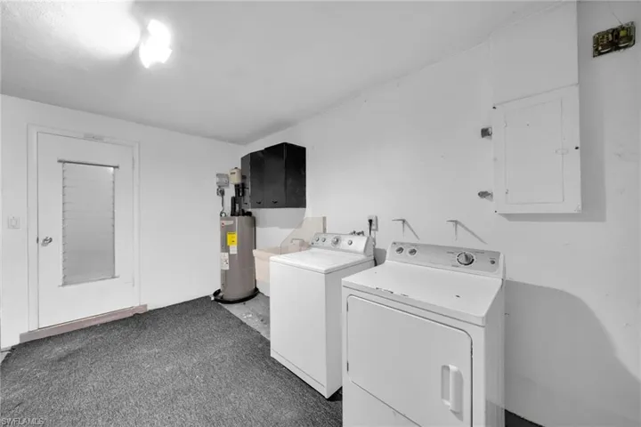 Laundry area featuring electric panel, water heater, washer and dryer, and dark colored carpet