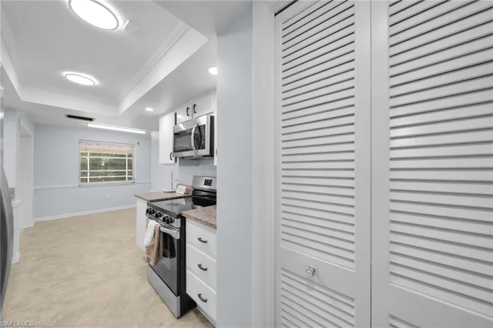 Kitchen with a tray ceiling, ornamental molding, appliances with stainless steel finishes, white cabinets, and recessed lighting