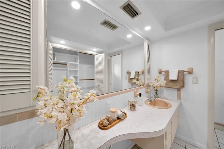 Bathroom featuring a closet, decorative backsplash, vanity, recessed lighting, and a tray ceiling