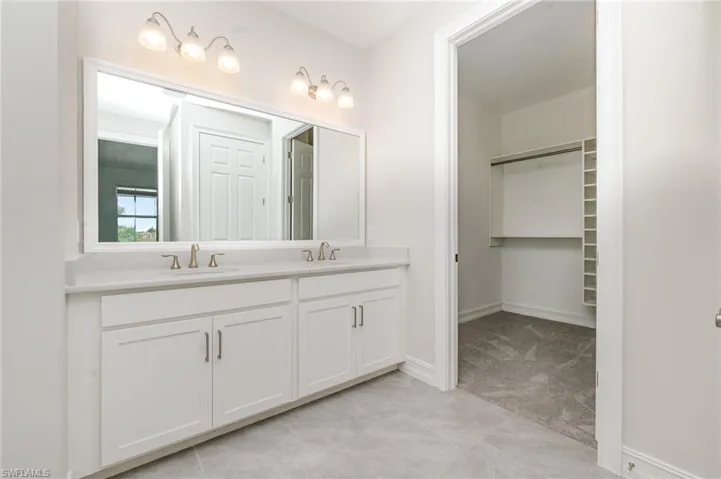 Bathroom featuring double vanity, a walk in closet, and light carpet