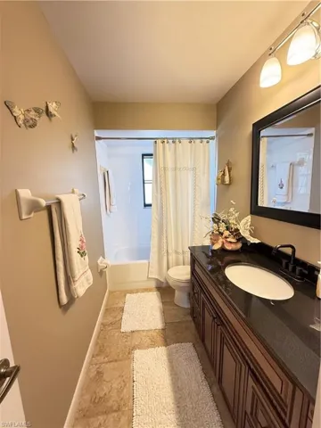 Bathroom with vanity, shower / tub combo with curtain, and light stone finish flooring